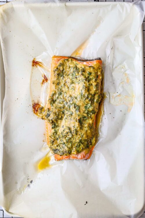 Salmon fillet topped with herb butter and lemon on parchment paper.