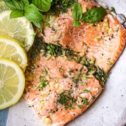 Fresh baked salmon with garlic, herbs, and lemon slices garnished with basil and dill.