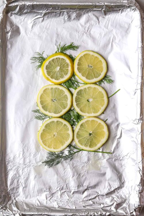 Lemon slices with fresh dill on aluminum foil for baking or cooking.