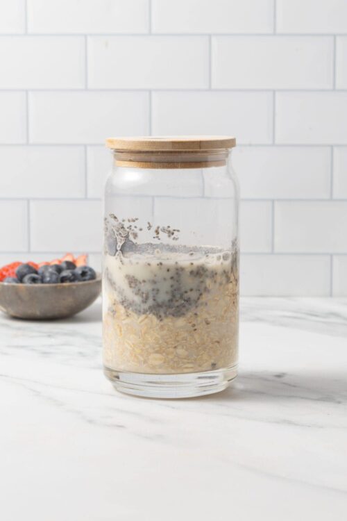 Oatmeal with chia seeds in glass jar with wooden lid on marble surface.