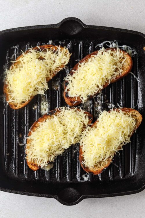 Golden brown garlic bread topped with shredded cheese in a cast iron skillet.