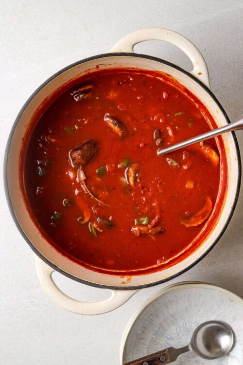 Savory mushroom and green pepper tomato soup in a white enameled pot.