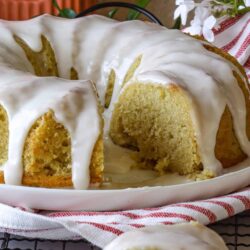 Butter cake with white glaze and sliced piece on plate.