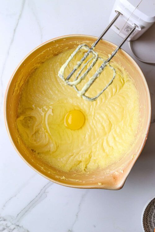 Creamy yellow cake batter with an egg in a mixing bowl, ready to be baked.