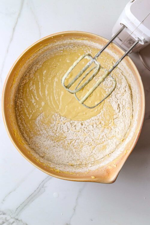 Flour and batter mixture in mixing bowl with electric hand mixer whisks, baking process, baking ingredients, preparation.