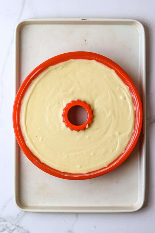 Cream cheese frosting spread in a round cake pan with a hollow center on a baking tray.