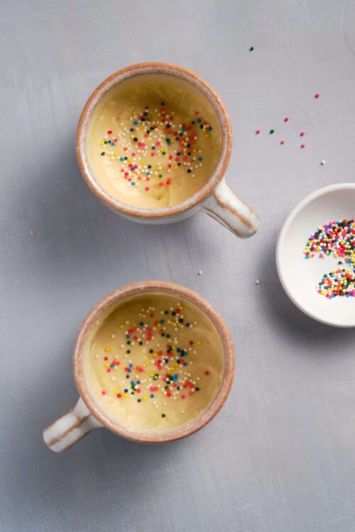 Colorful sprinkle-topped cupcake batter in rustic mugs, ready for baking or decorating, perfect for fun desserts.