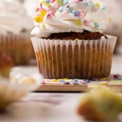 Colorful sprinkle-topped cupcake with white frosting on a baking paper; bakery dessert photo.