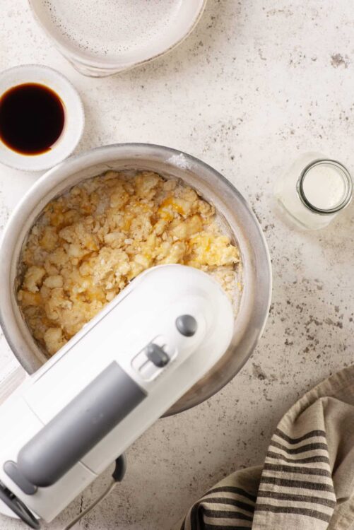 Creamy mashed potato mixture being prepared in a stand mixer with ingredients around.
