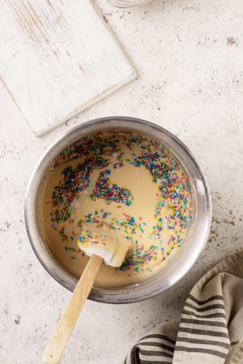 Rainbow sprinkles in vanilla cake batter, baking, dessert preparation, baking ingredients, colorful sprinkles for cake decorating.