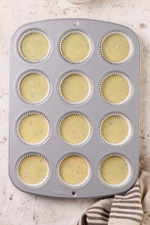 Mini cupcake batter in colorful specks in cupcake liners in a baking pan.