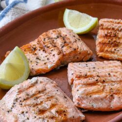 Salmon fillets with lemon wedges on a rustic plate, seasoned for grilling or baking.