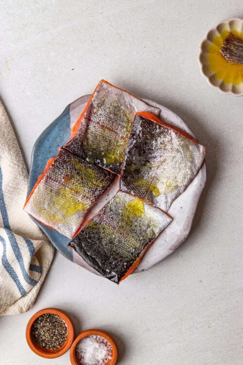 Fresh salmon fillets with crispy skin on a white plate, ready for cooking or baking.