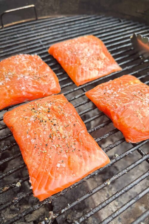 Fresh salmon fillets grilled with salt and pepper on cooking grate.