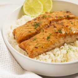 Salmon with lemon and herbs served over white rice, garnished with fresh herbs and lemon slices.