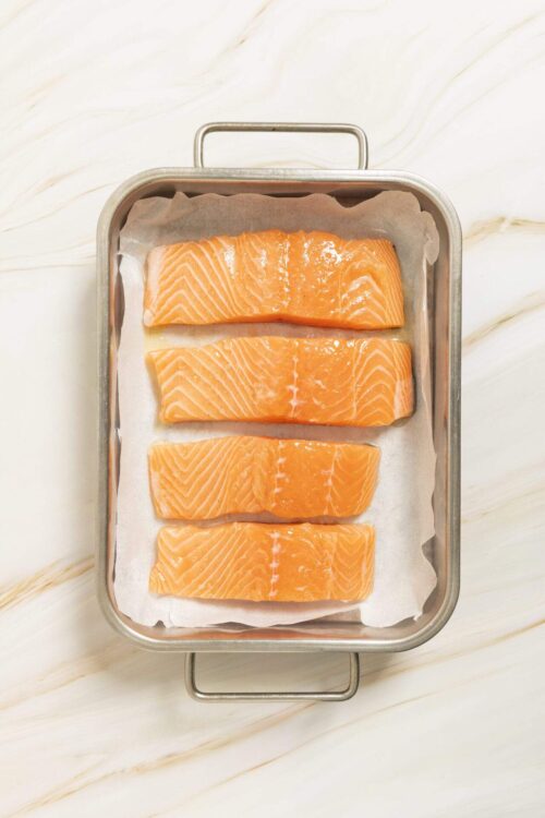Fresh salmon fillets prepared for baking on a parchment-lined baking sheet.