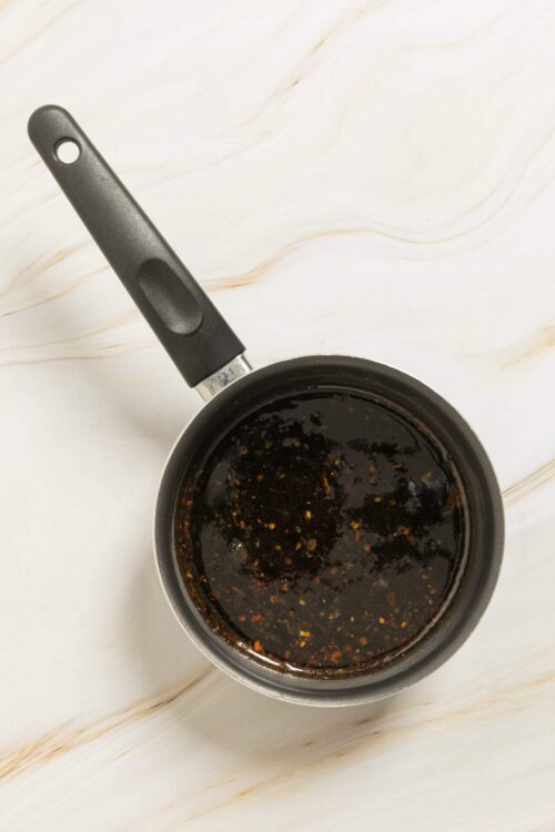 Soy sauce or teriyaki sauce in a small saucepan on white marble surface.