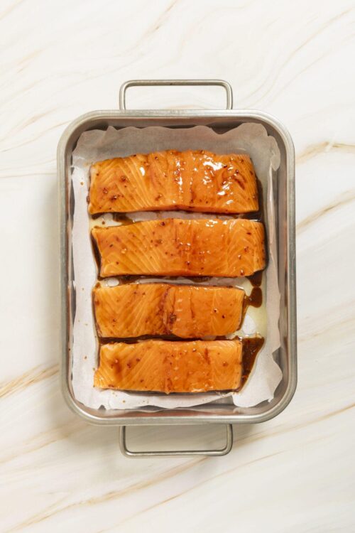 Salmon fillets marinated with soy sauce in a baking dish on parchment paper.