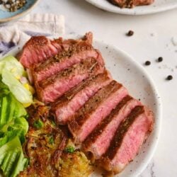 Juicy medium-rare steak with crispy hash browns and fresh salad on white ceramic plate.