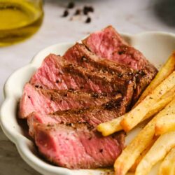 Juicy grilled steak with crispy French fries on a white plate. Perfectly cooked beef served with golden fries and seasoned with pepper.
