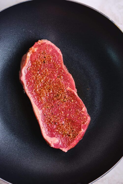 Raw steak in a sizzling cast iron skillet, seasoned steak ready to cook, high-quality beef steak in frying pan, best steak recipe, cooking seasoned beef steak.