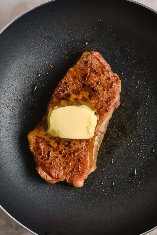 Searing seasoned steak in a black skillet with melting butter, ready for finishing or serving.