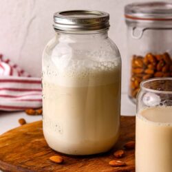 Homemade almond milk in a glass jar with almonds scattered around on a wooden board.