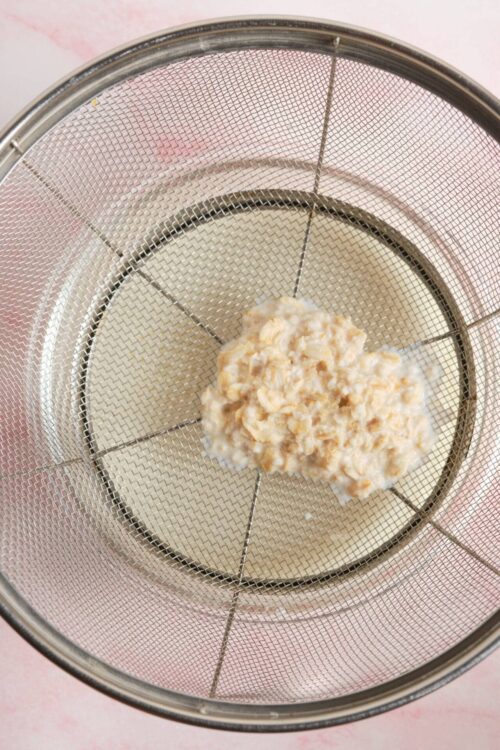 Cream cheese and shredded cheese mixture in a fine mesh sieve, used for baking or cheese blending.