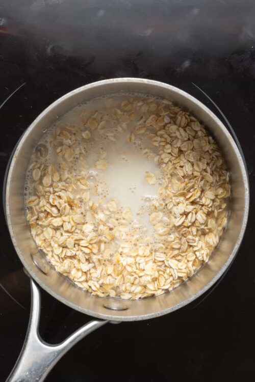Oats soaking in milk in a stainless steel pan for baking oats or oatmeal dish.