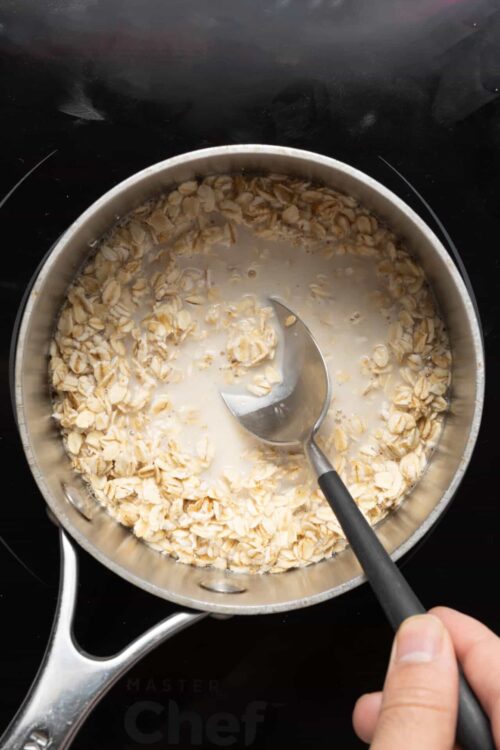 Oatmeal cooking in a pot with a ladle, creamy texture, home baking, breakfast recipe, wholesome ingredients.