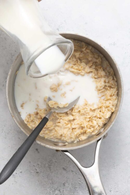 Cream being poured into a potato mixture in a metal pan on a light surface.