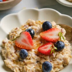 Creamy oatmeal topped with strawberries and blueberries in a white bowl.