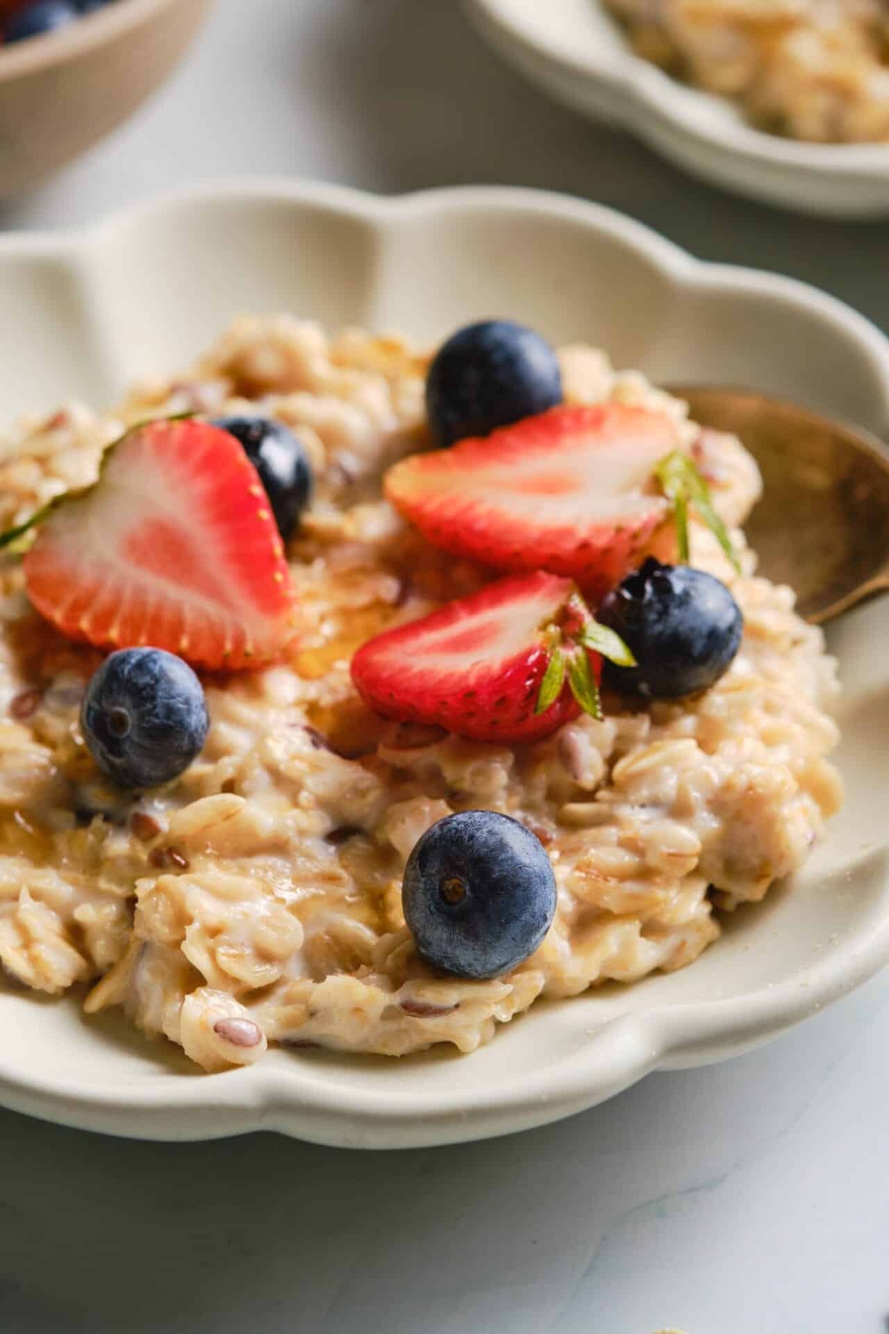 Creamy oatmeal topped with fresh strawberries and blueberries in a decorative white bowl.