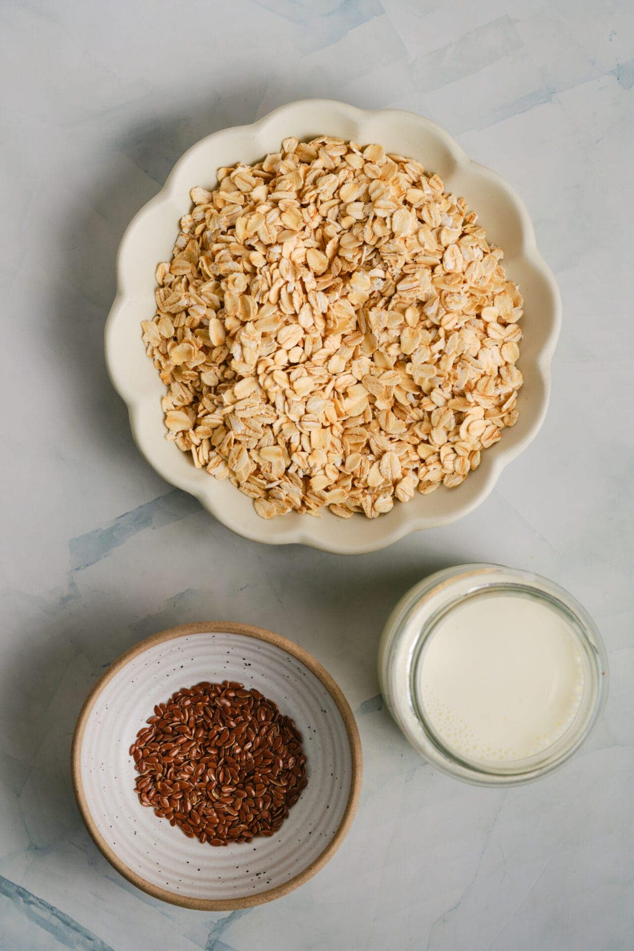 Crunchy rolled oats and flax seeds in a white bowl with fresh milk on a marble surface.