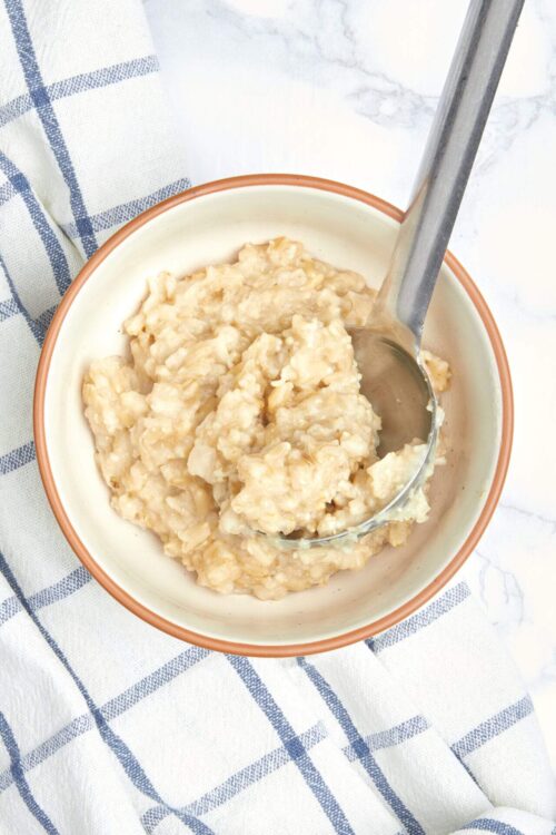 Creamy homemade mashed bananas in a white bowl on a white and blue checkered cloth.