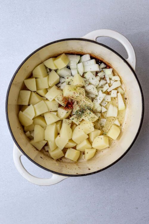 Creamy potato stew with chopped potatoes, onions, herbs, and spices cooking in a Dutch oven.