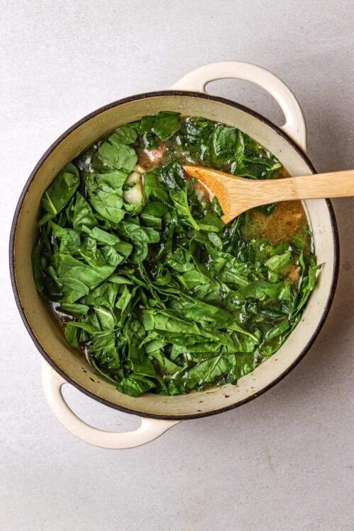 Fresh sautéed spinach in a creamy garlic sauce in a Dutch oven with a wooden spoon.