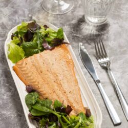 Fresh baked salmon with mixed greens on a white platter, served with water and a glass of white wine.