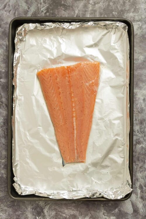 Baked salmon fillet on foil-lined baking sheet ready to roast.