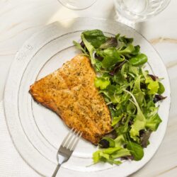 Grilled salmon with fresh green salad on white plate, served with water and wine.