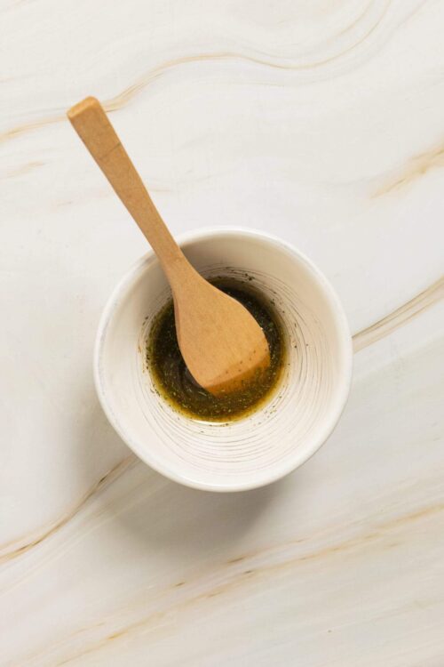 Savory herb-infused olive oil in a white bowl with a wooden spoon, perfect for cooking or dipping bread.