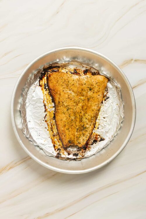 Baked salmon fillet on foil-lined baking dish, cooked to perfection with herbs.