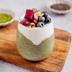 Delicious chia seed pudding with whipped cream topped with mixed berries and nuts, served on a wooden board.