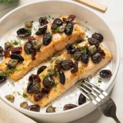 Succulent baked salmon with olive tapenade on a white dish, garnished with fresh herbs.