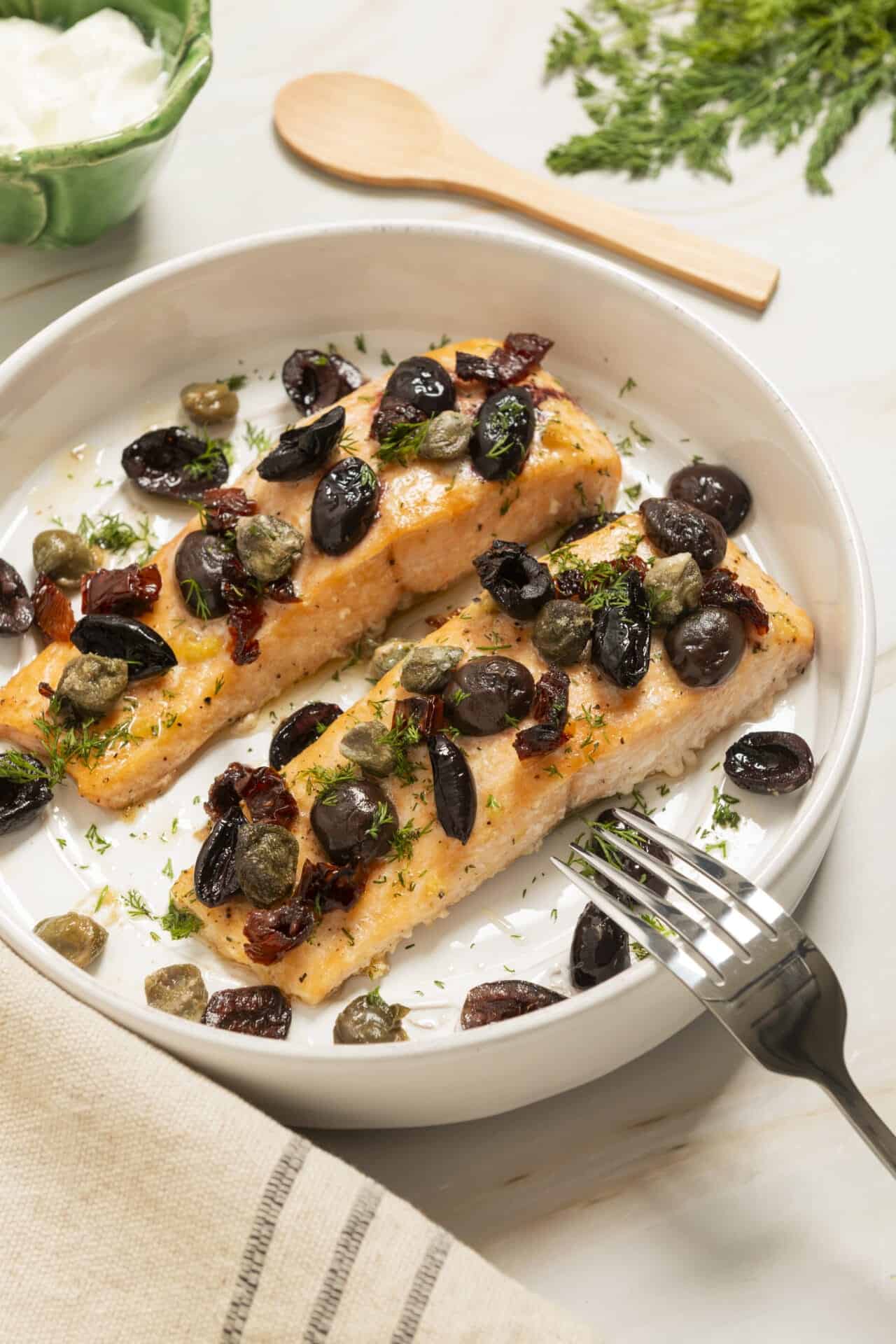 Succulent baked salmon with olive tapenade on a white dish, garnished with fresh herbs.