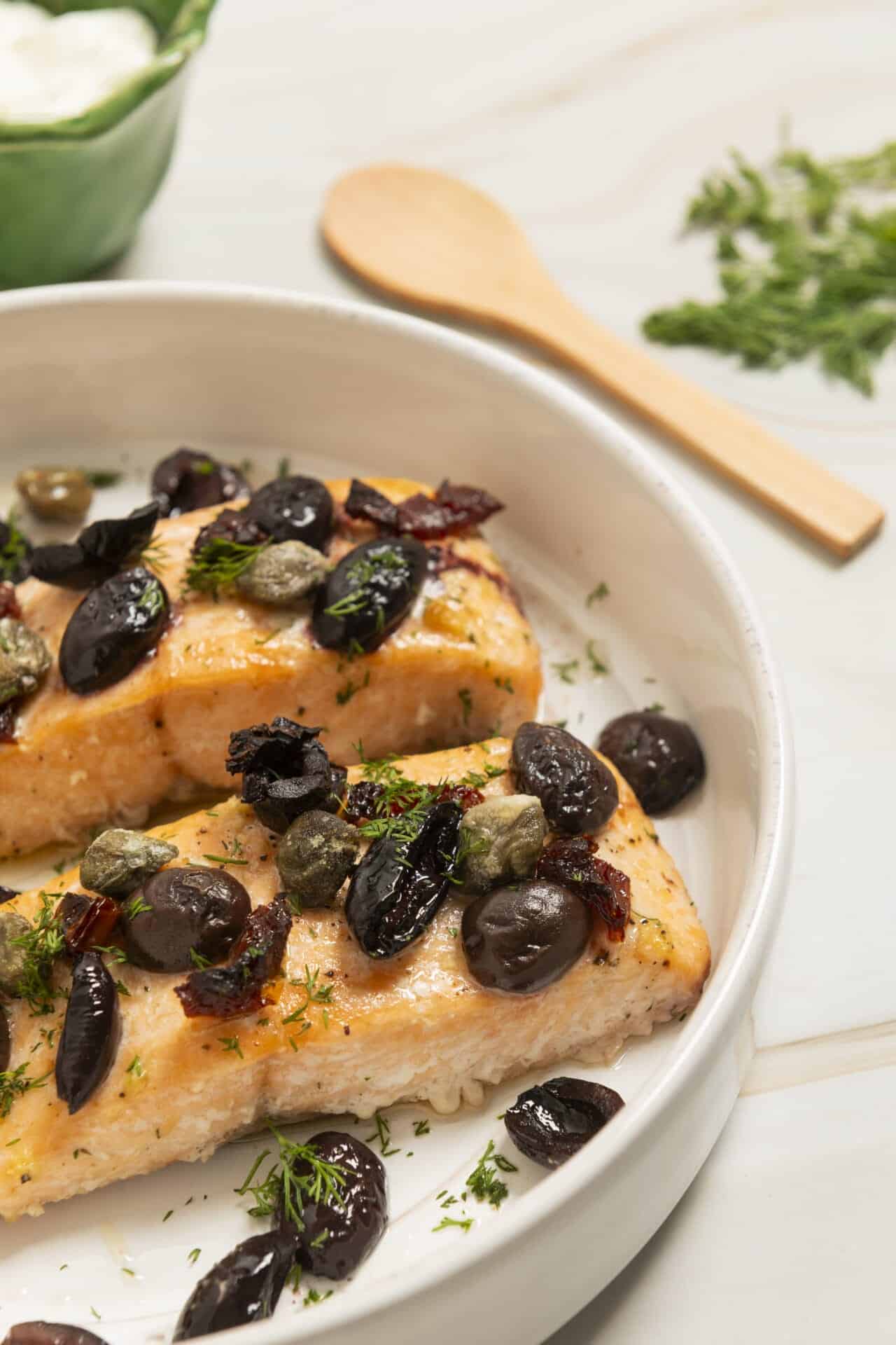 Succulent baked salmon with black olives and fresh herbs in a white baking dish.
