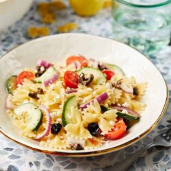 Creamy pasta salad with cherry tomatoes, cucumbers, red onions, and black olives, garnished with feta cheese. Perfect for picnics and summer meals.