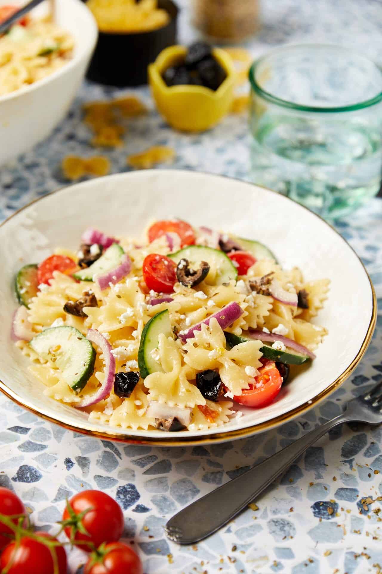 Creamy pasta salad with cherry tomatoes, cucumbers, red onions, and black olives, garnished with feta cheese. Perfect for picnics and summer meals.