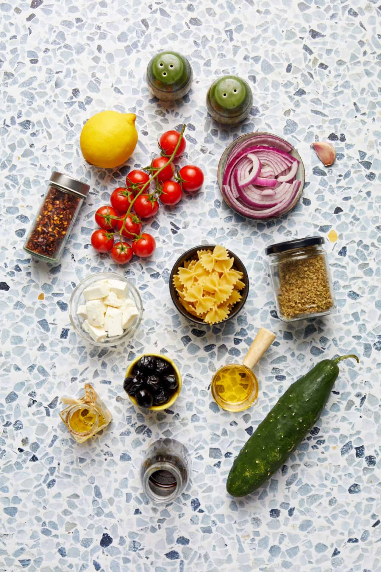 Fresh vegetable and pasta ingredients for Italian cooking on terrazzo surface.