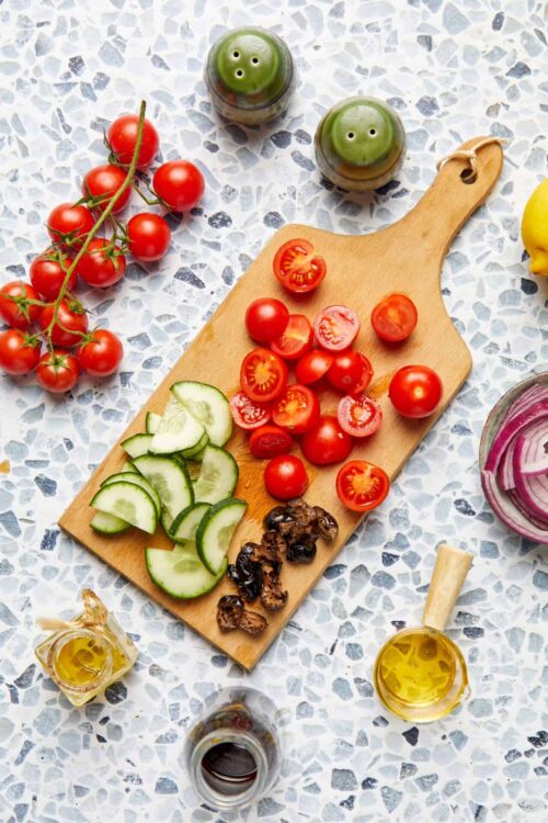 Juicy cherry tomatoes, sliced cucumbers, and balsamic vinegar on a wooden cutting board.